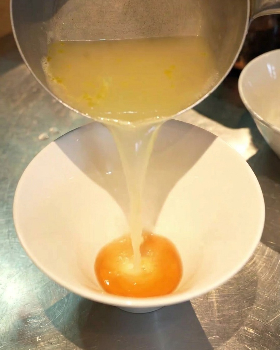 Un filet de bouillon de poulet doré versé dune casserole argentée dans un bol blanc contenant le tare.
