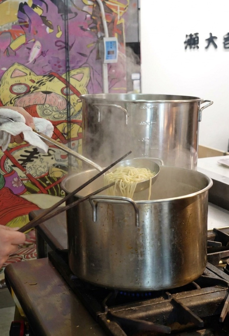 Une personne utilisant une passoire pour sortir les nouilles ramen cuites dune grande marmite deau.
