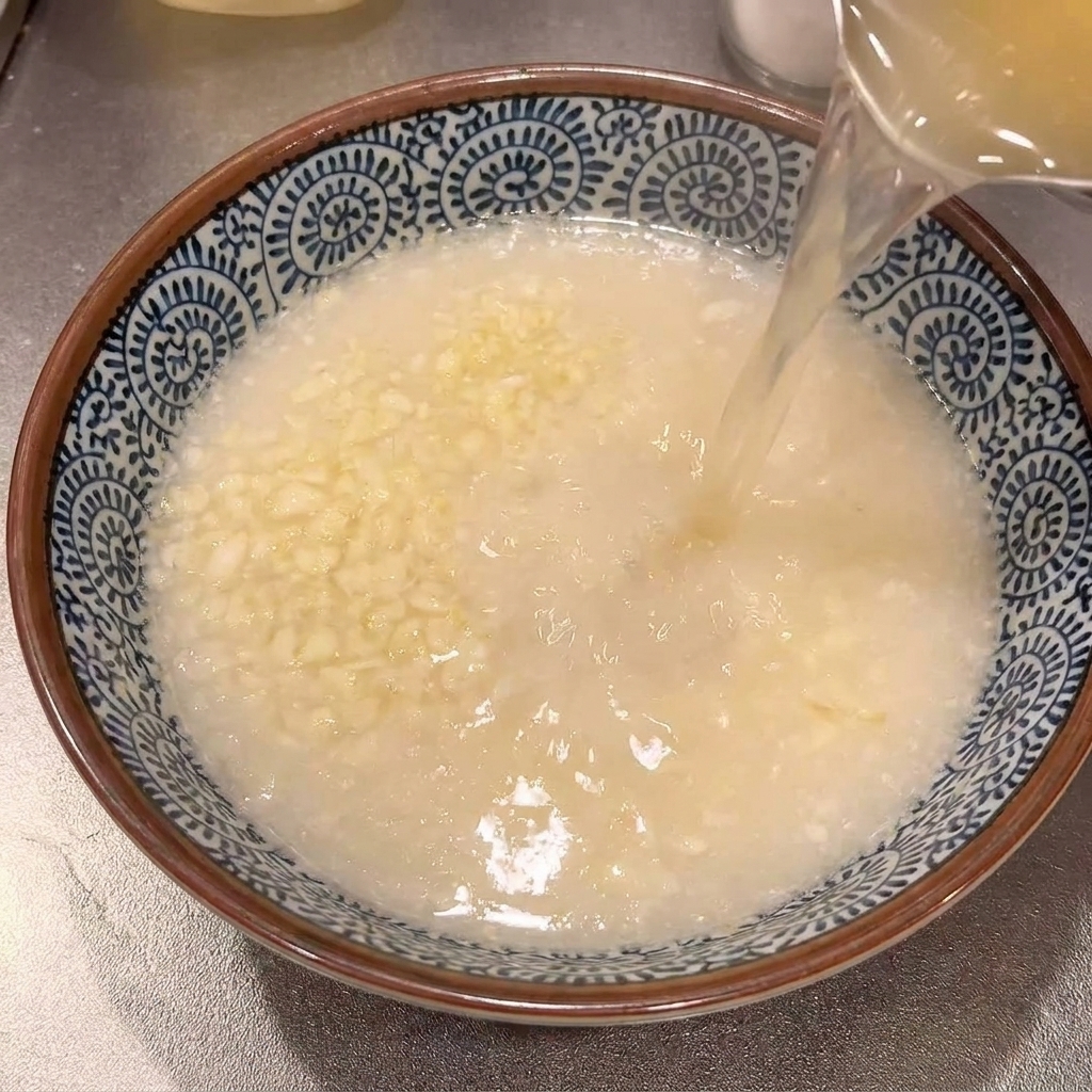 Bouillon de ramen chaud et clair versé dune casserole dans un bol en céramique contenant lail râpé.