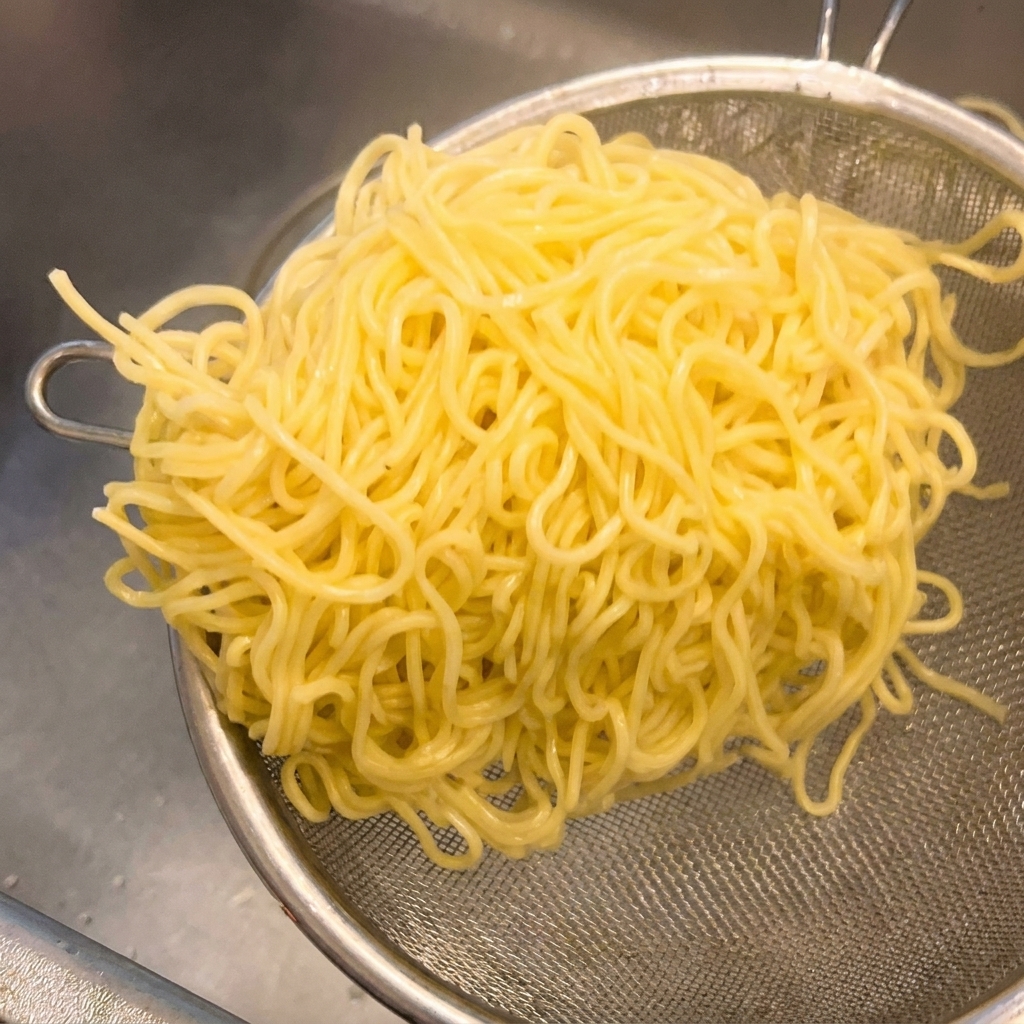 Nouilles ramen jaunes dans une passoire métallique secouée pour éliminer lexcédent deau de cuisson.