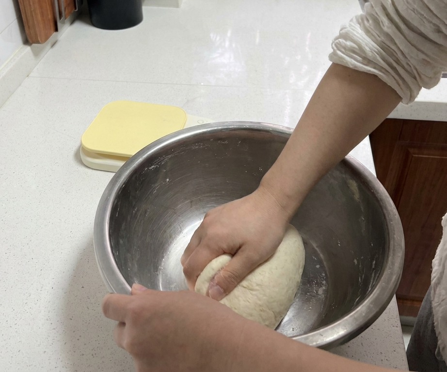 Mains pétrissant fermement une boule de pâte blanche dans un bol mélangeur en métal sur un plan de travail propre.