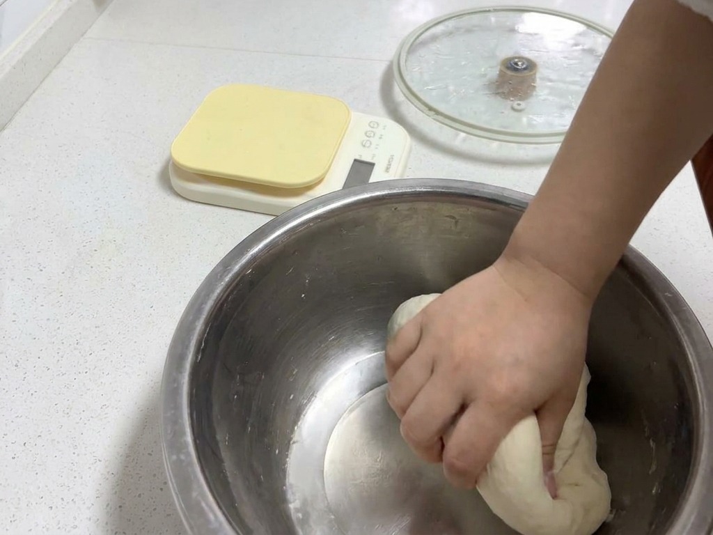 Une main pétrissant une boule de pâte lisse et ronde dans un bol en métal pour développer une texture élastique.
