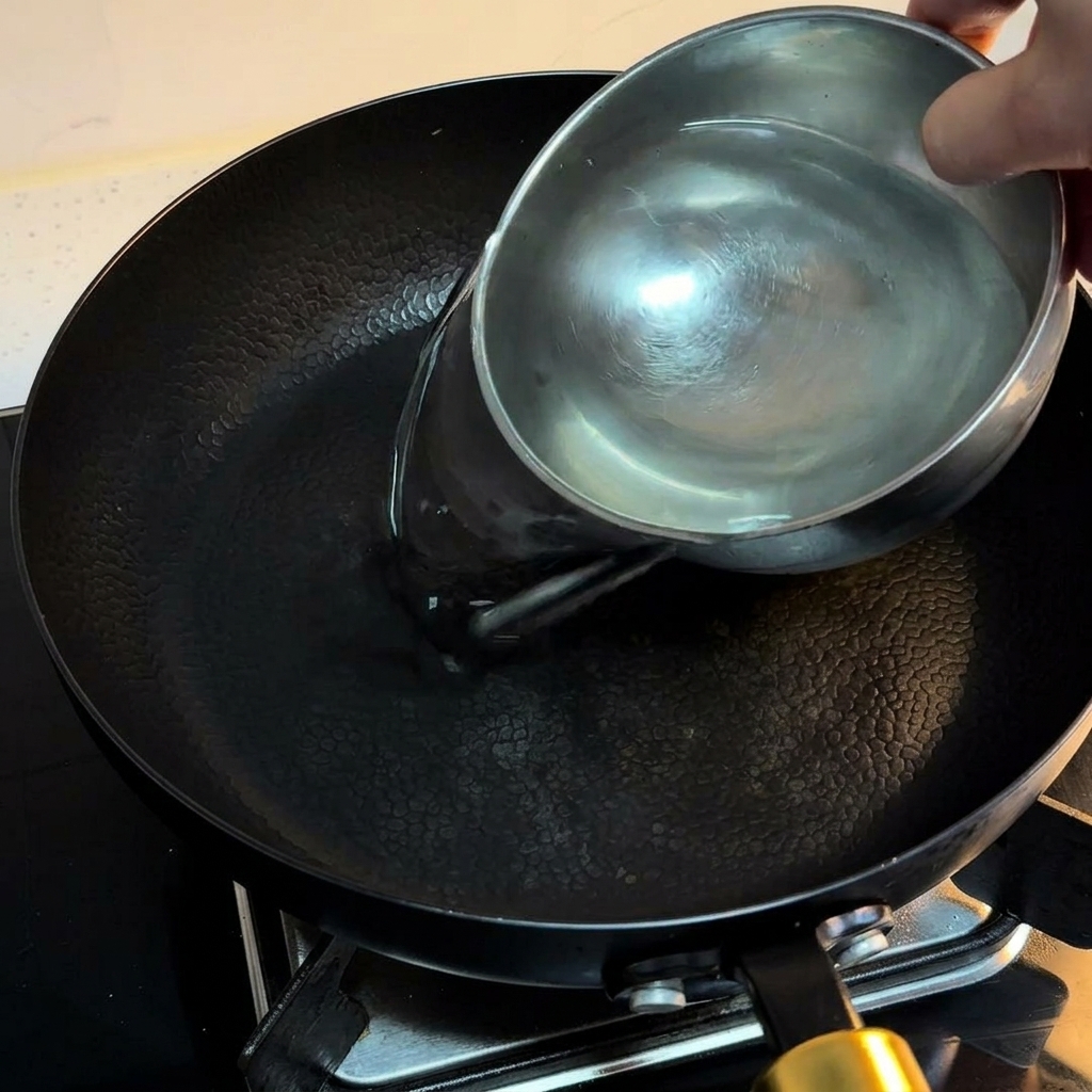 Eau versée dun bol en acier inoxydable dans une poêle antiadhésive noire sur une cuisinière.