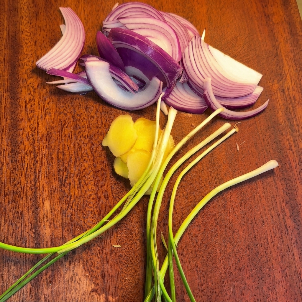 Planche à découper avec des lamelles doignon rouge, des rondelles de gingembre et des tiges doignons verts frais.