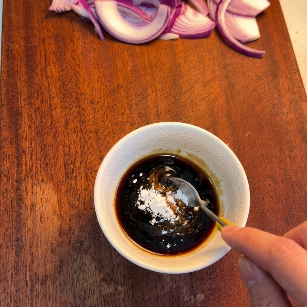 Une cuillère mélangeant une sauce brun foncé dans un bol blanc pour y dissoudre de la fécule blanche.