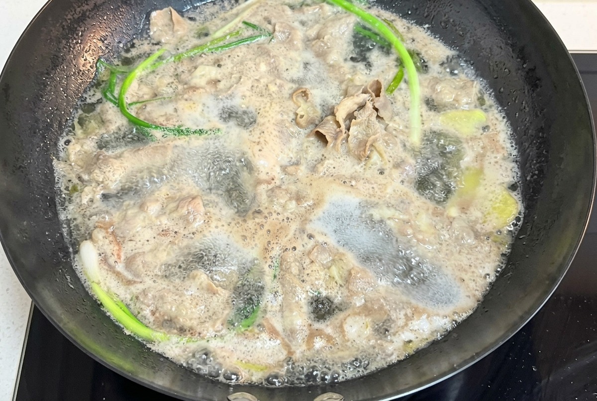Fines tranches de bœuf bouillant dans une casserole deau avec de longues tiges doignons verts.