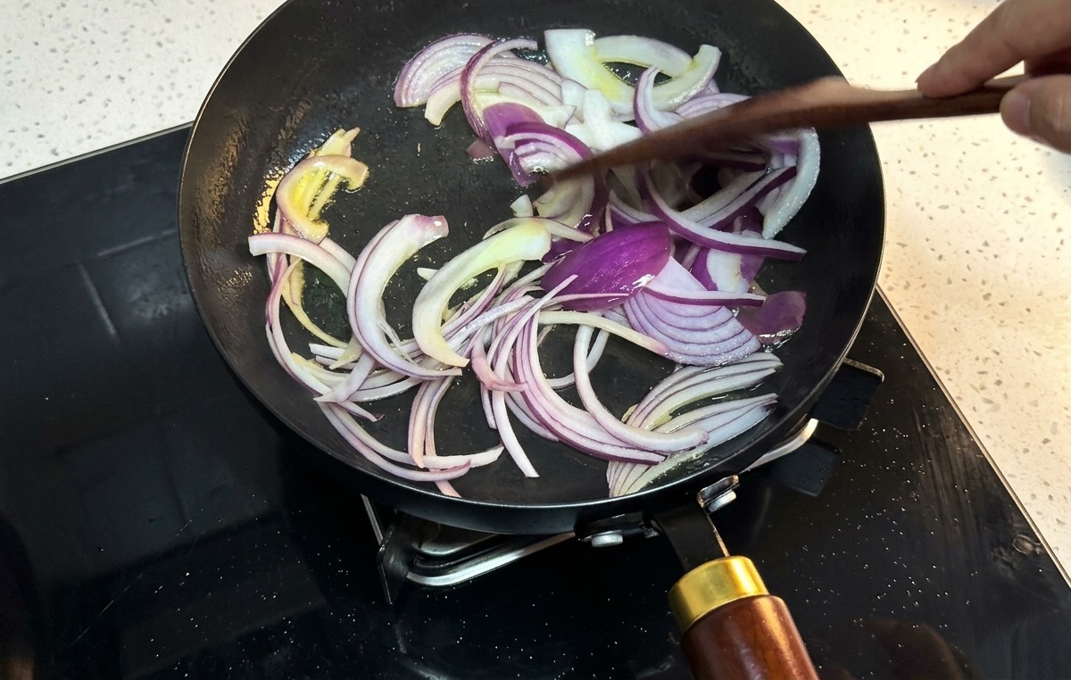 Lamelles doignon rouge remuées avec une spatule en bois dans une poêle à frire noire.