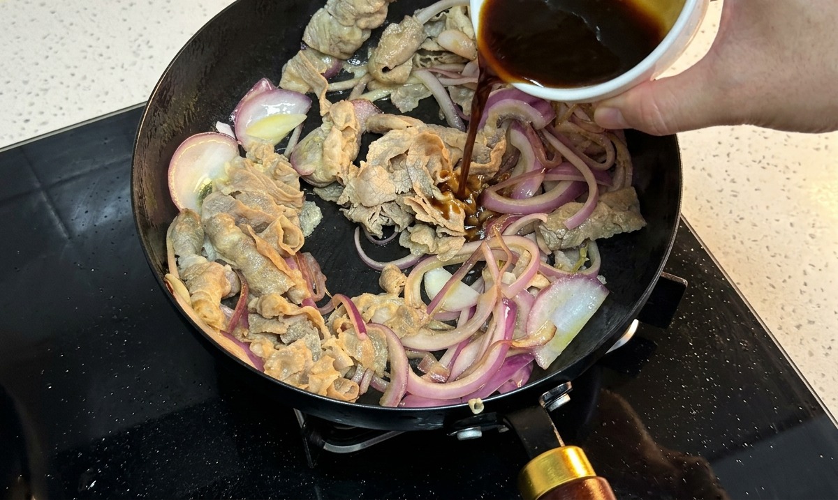 Sauce sombre versée dun bol en céramique blanche dans une poêle contenant le bœuf et les oignons.