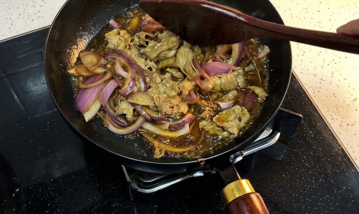 Bœuf et oignons rouges mijotant dans une sauce sombre, épaisse et bouillonnante, remués avec une spatule.