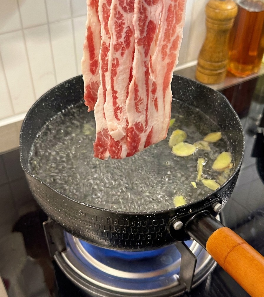 Fines tranches de bœuf cru ajoutées à une casserole deau bouillante contenant des tranches de gingembre.