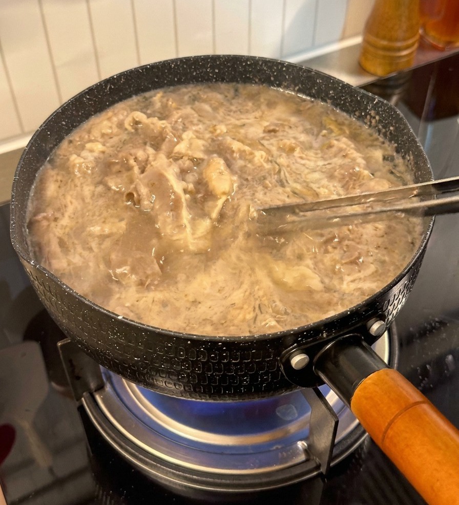 Tranches de bœuf soulevées hors de leau bouillante avec des pinces, paraissant pâles et pré-cuites.