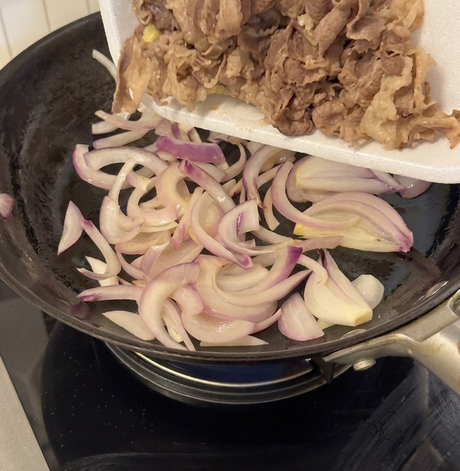 Bœuf blanchi versé dun plateau blanc dans une poêle contenant les oignons sautés.