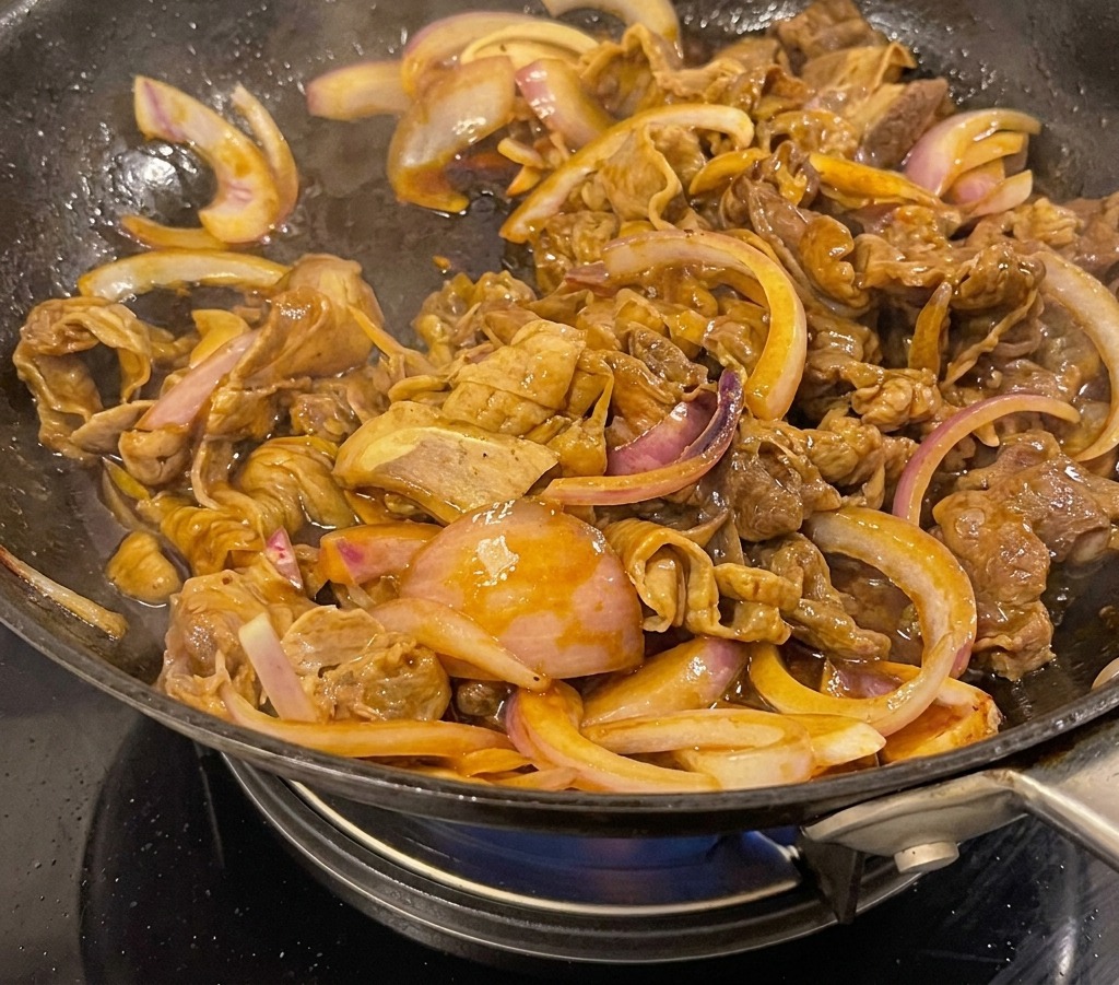 Bœuf teriyaki et oignons mijotant dans une sauce brune épaisse et brillante dans un wok noir.