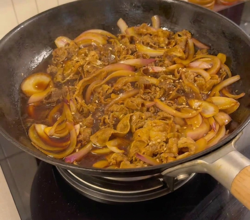 Bœuf teriyaki terminé dans la poêle, garni de graines de sésame blanc et doignons verts ciselés.