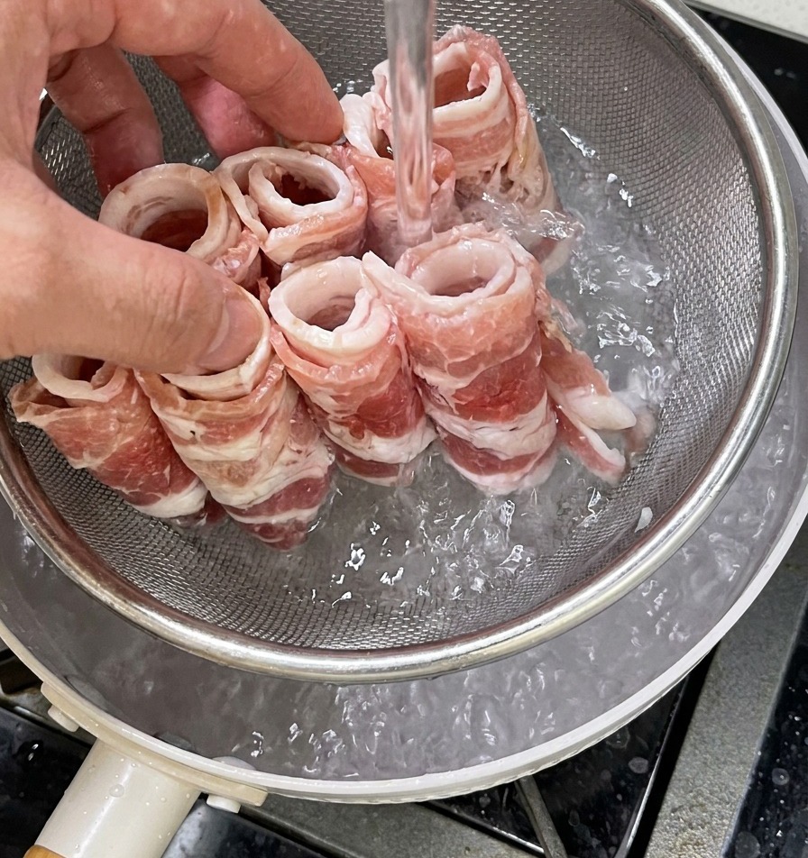 Rouleaux de bœuf déposés dans une passoire et plongés dans une casserole deau bouillante.