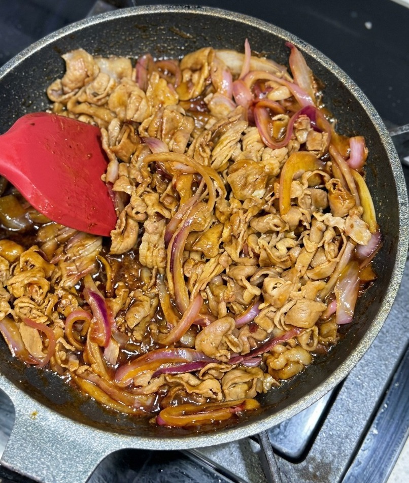 Bœuf et oignons enrobés dun glaçage brun épais et scintillant dans la poêle.