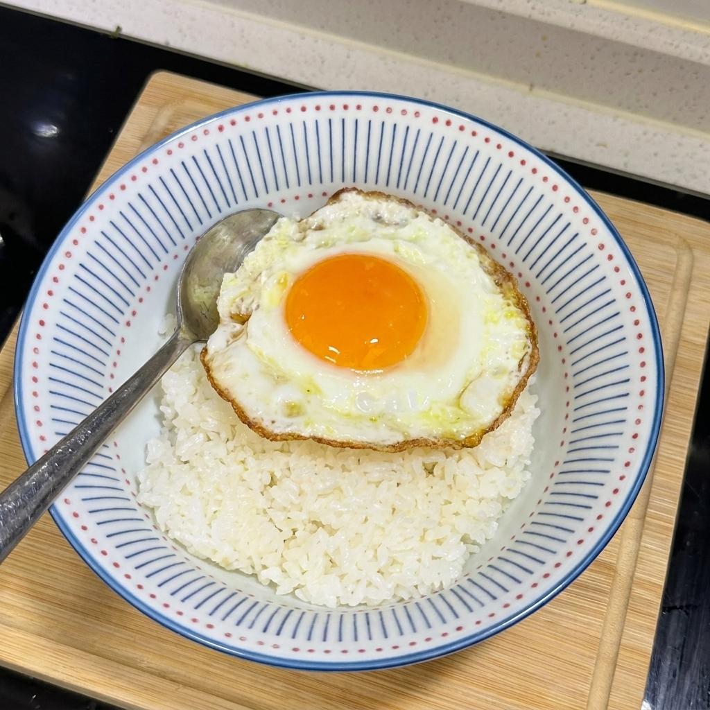 Vue de dessus dun bol de riz surmonté dun œuf au plat au jaune coulant et aux bords croustillants.