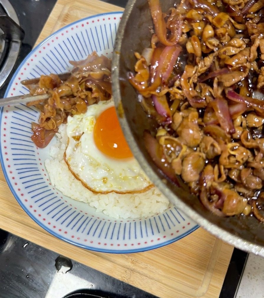 Bœuf teriyaki et oignons versés depuis la poêle sur le bol de riz et dœuf.