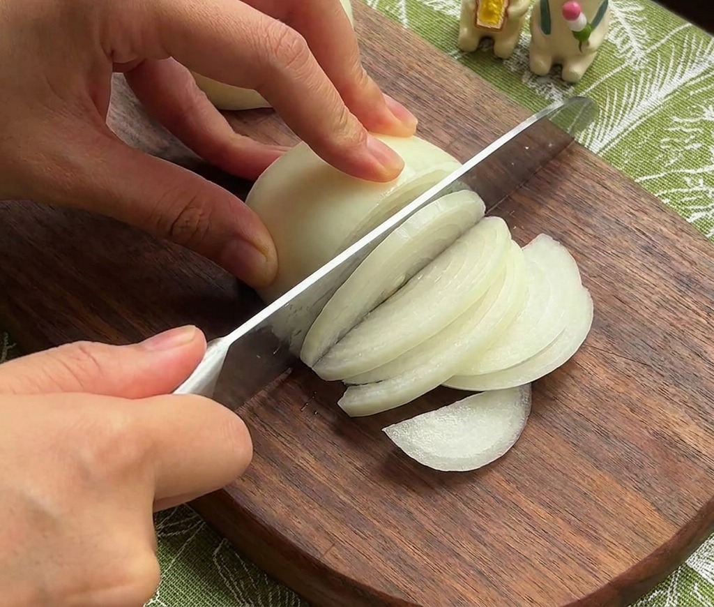 Une personne utilisant un couteau de chef pour couper un oignon blanc en fines lanières sur une planche à découper en bois.