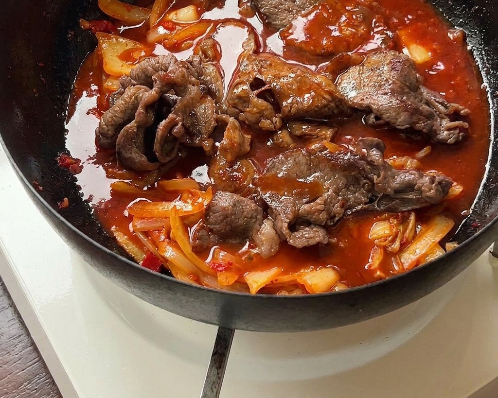 Le mélange de bœuf et kimchi mijotant dans une sauce rouge épaisse et brillante dans une poêle en fer.