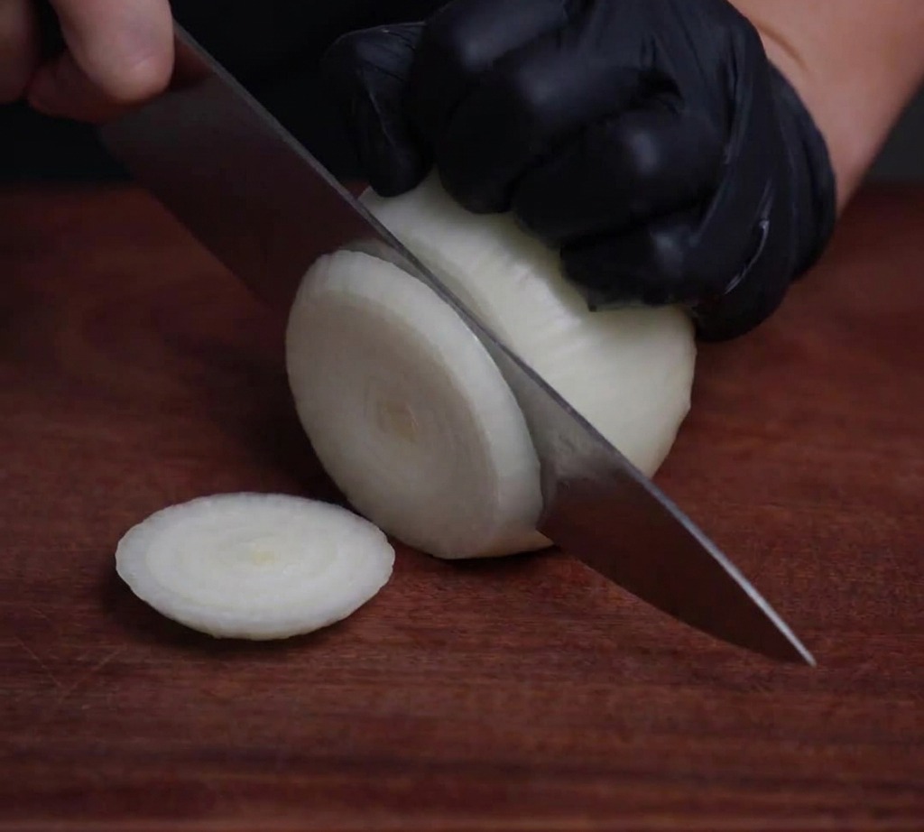 Un oignon blanc coupé en fines rondelles translucides sur une surface en bois à laide dun couteau de chef professionnel.