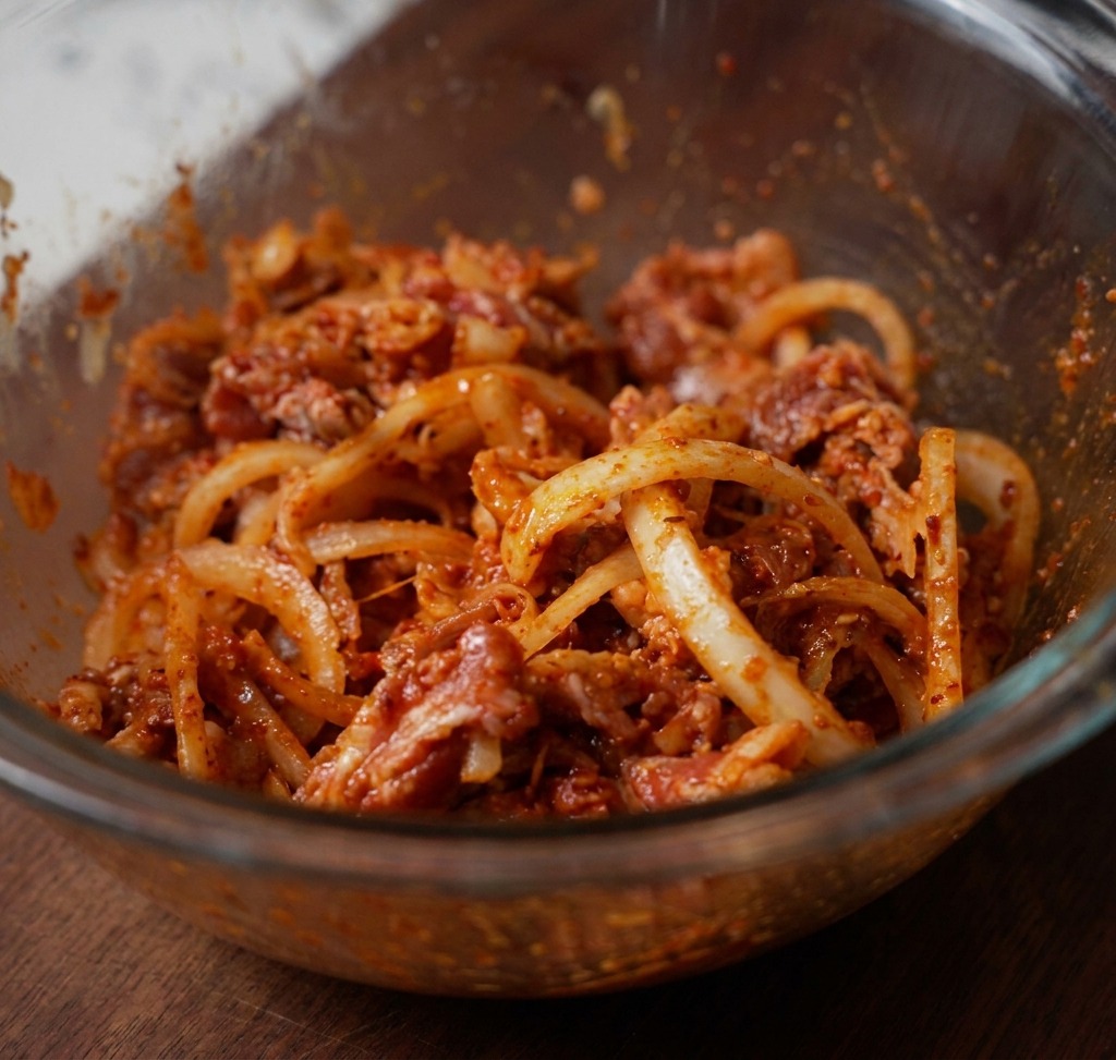 Tranches de bœuf, oignons blancs et pâte de piment rouge soigneusement mélangés dans un bol en verre transparent.