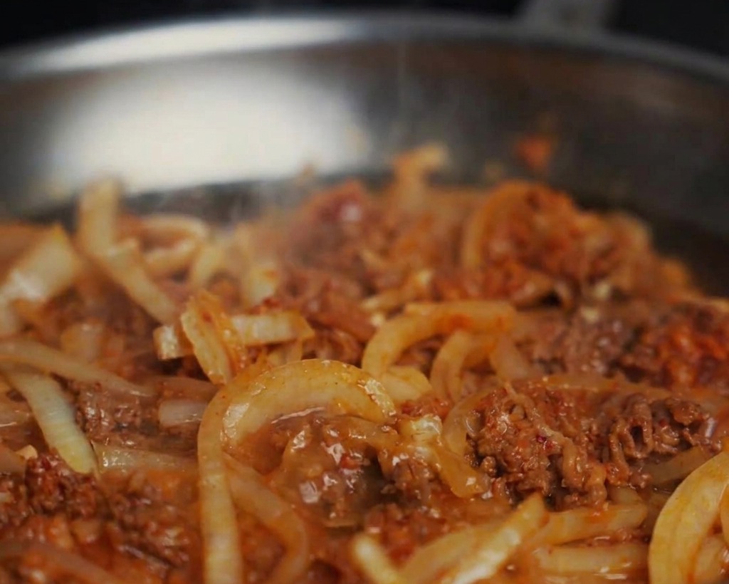 Eau ajoutée à une poêle de bœuf sauté et doignons, créant une sauce bouillonnante.
