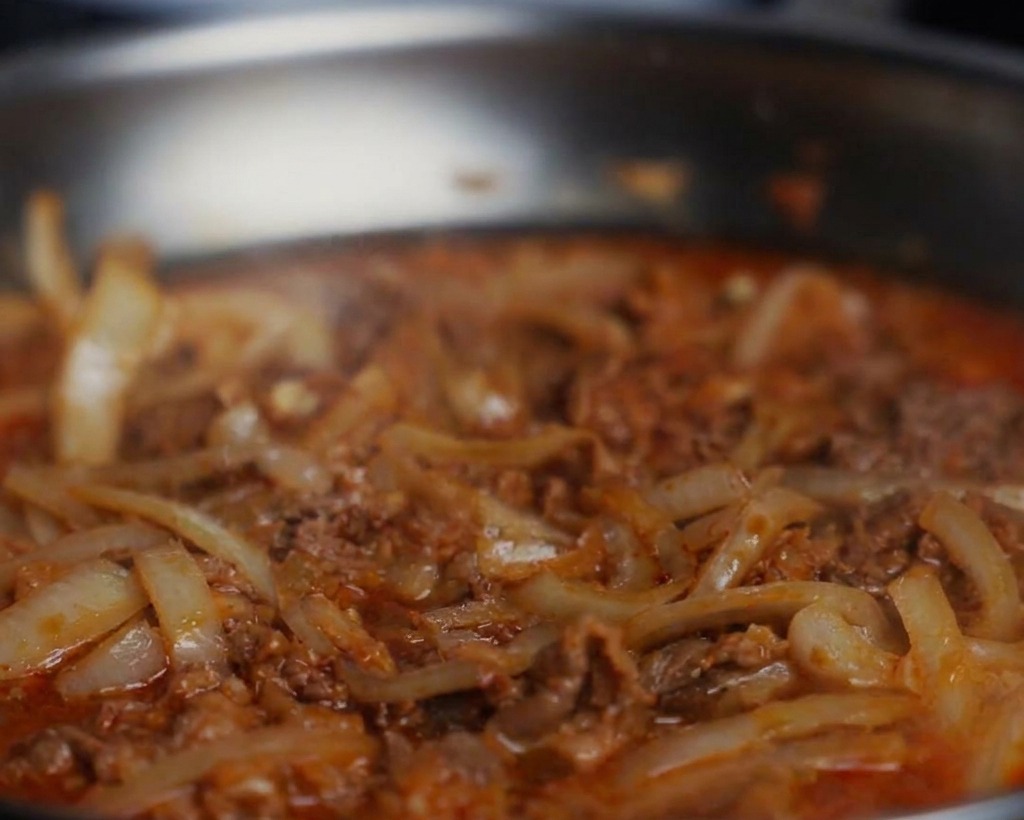 Gros plan sur du poivre noir et de la sauce soja ajoutés dans une poêle frémissante de bœuf et doignons.