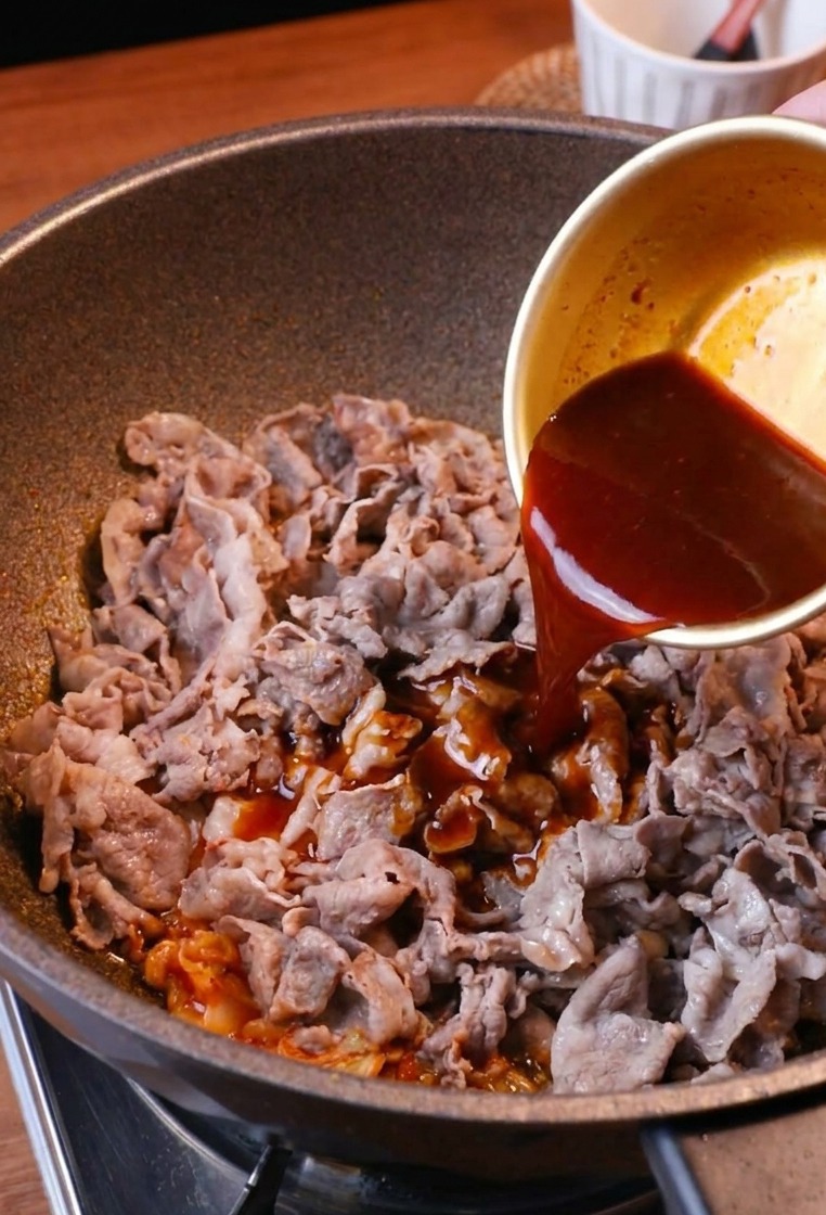 Une sauce brun-rouge savoureuse versée depuis un bol sur le sauté de bœuf au kimchi.