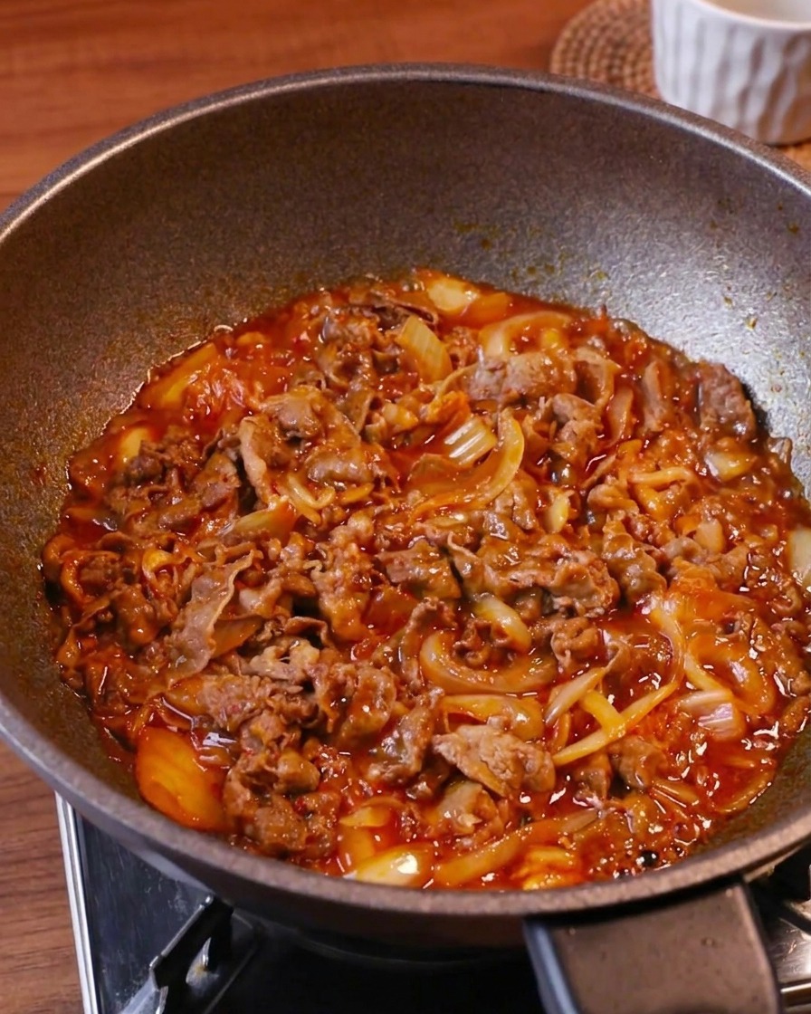 De tendres tranches de bœuf, du kimchi et des oignons mijotant dans une sauce rouge bouillonnante dans un wok à feu vif.