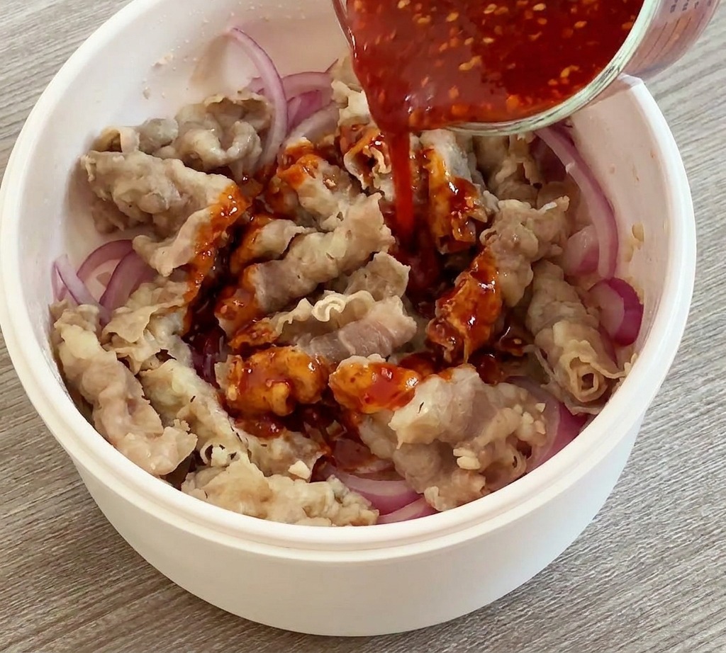 Versement dune sauce rouge vive depuis un verre doseur sur le bœuf et les oignons dans une poêle.