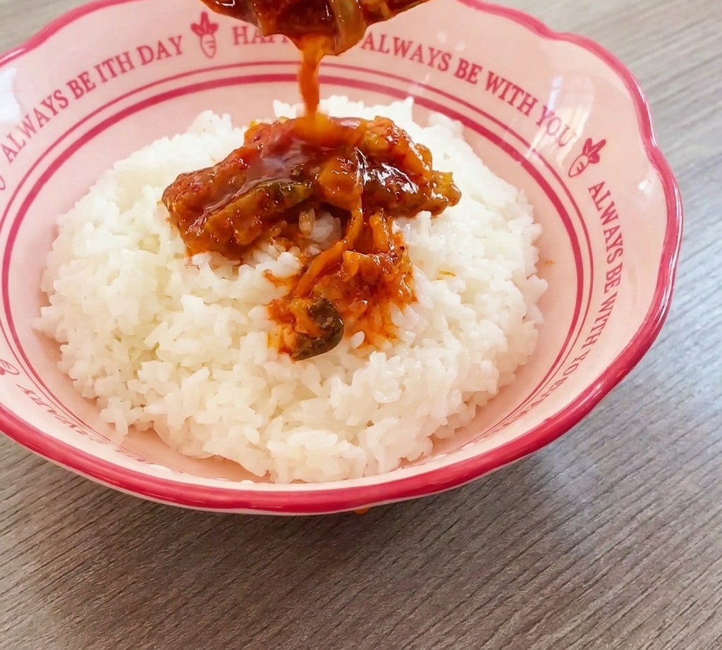 Mélange savoureux de bœuf et kimchi versé à la cuillère sur un dôme de riz blanc dans un bol rose.