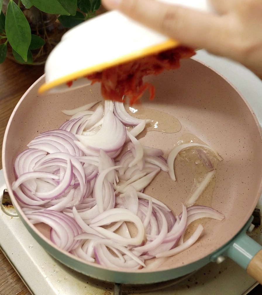 Poêle en céramique rose contenant des oignons rouges émincés et du kimchi rouge épicé.