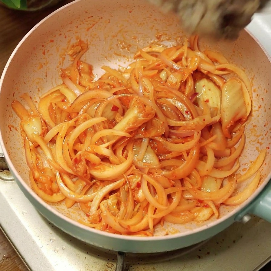 Le bœuf cuit ajouté aux oignons et au kimchi dans la poêle rose.