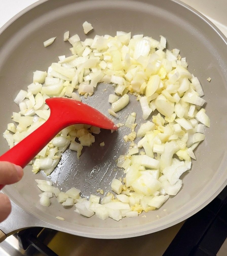 Dés doignon et ail sautant dans une poêle grise avec une spatule en silicone rouge.