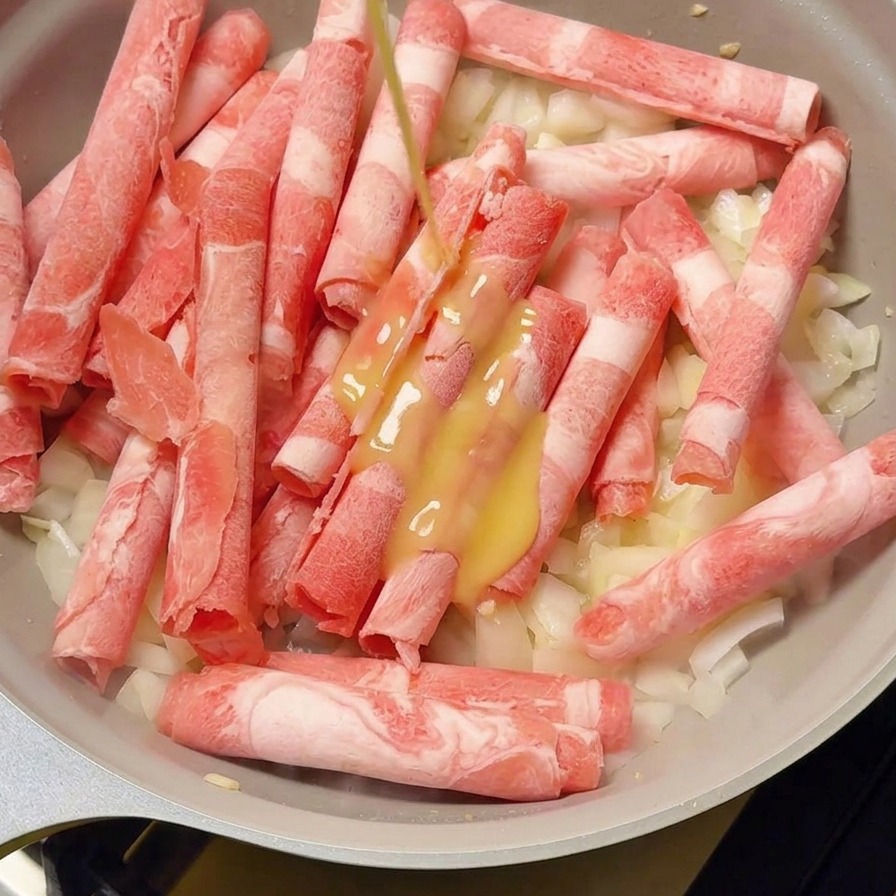 Jus de gingembre versé dune petite bouteille sur le bœuf et les oignons dans la poêle.