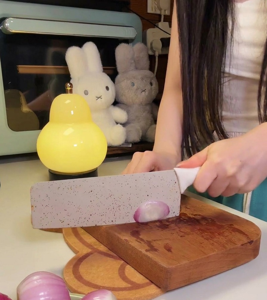 Une personne utilisant un couteau de cuisine pour émincer finement des petits oignons rouges sur une planche en bois.