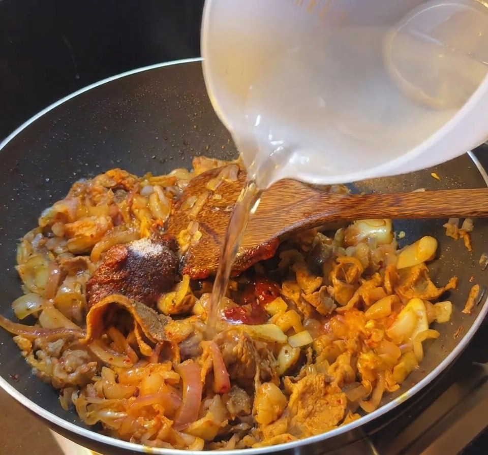 De leau claire versée dans une poêle contenant le bœuf et la sauce épicée au kimchi.