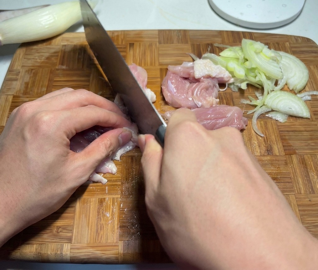 Un chef coupant de la chair rose de hauts de cuisse de poulet en morceaux de la taille dune bouchée sur une planche à découper.