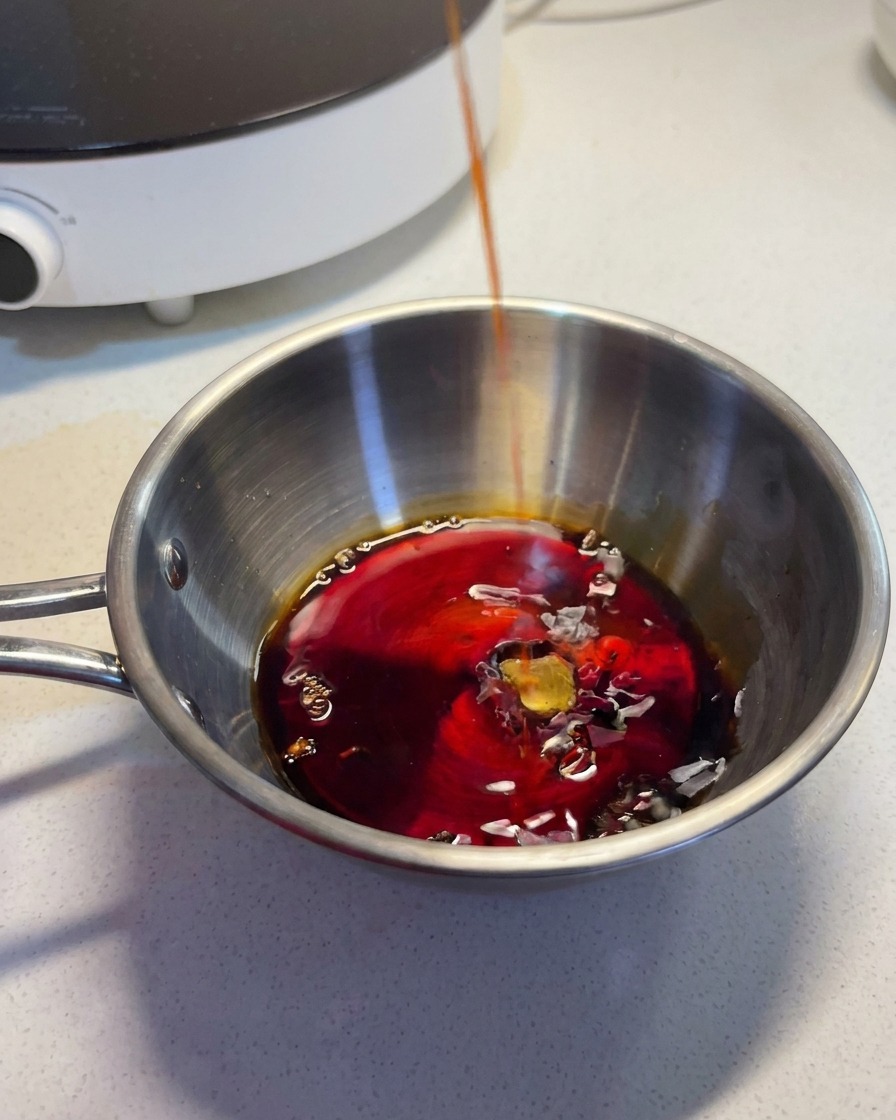 Un liquide sombre et savoureux versé dans un bol en inox contenant les autres ingrédients de la sauce.