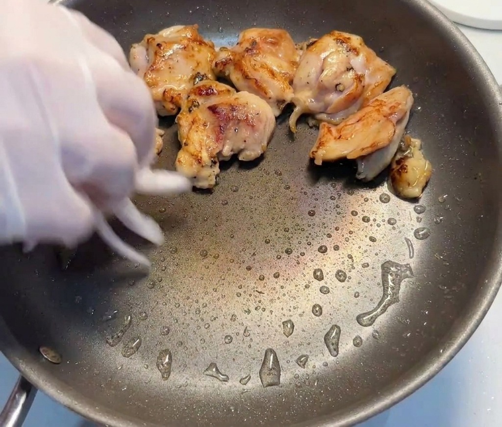 Lamelles doignons rouges ajoutées à la main dans une poêle contenant les morceaux de poulet saisis.