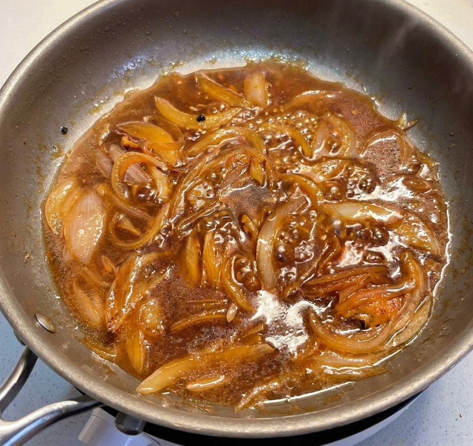 Rondelles de poireau vert ajoutées dans une sauce sombre bouillonnante avec des oignons fondants.
