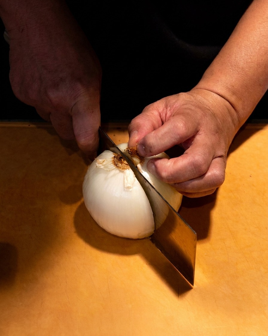 Gros plan de mains coupant soigneusement un oignon blanc en fines lamelles sur une planche en bois.