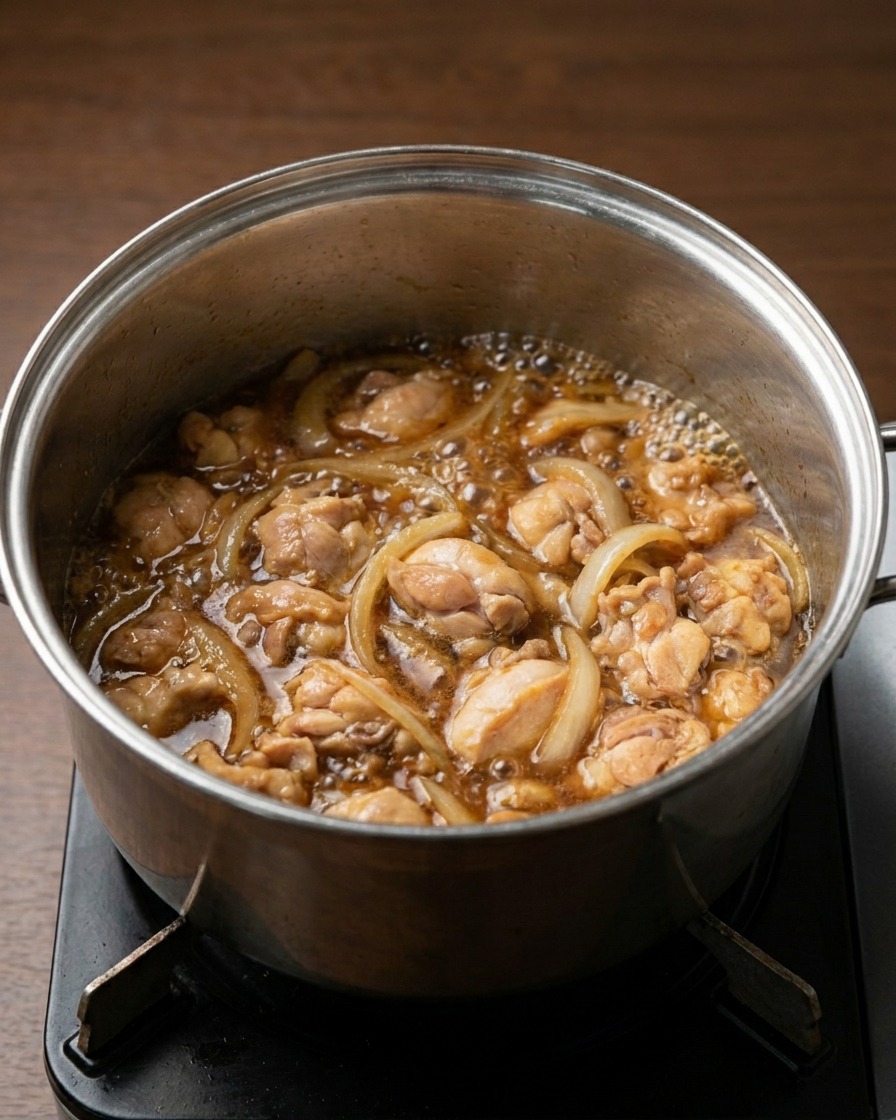 Une casserole sur le feu avec du poulet et des oignons mijotant dans un liquide brun foncé savoureux.