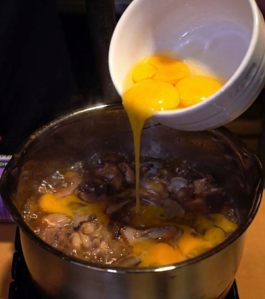 Blancs dœufs versés dun bol en céramique blanche dans une casserole de poulet et doignons mijotant dans une sauce foncée.