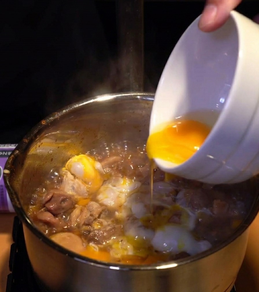 Jaunes dœufs dun jaune vif versés dun bol sur une couche de blancs cuits et de poulet dans une casserole frémissante.