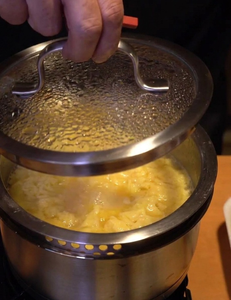 Gros plan dune main posant un couvercle en verre sur une casserole de poulet et dœufs pour les laisser figer hors du feu.