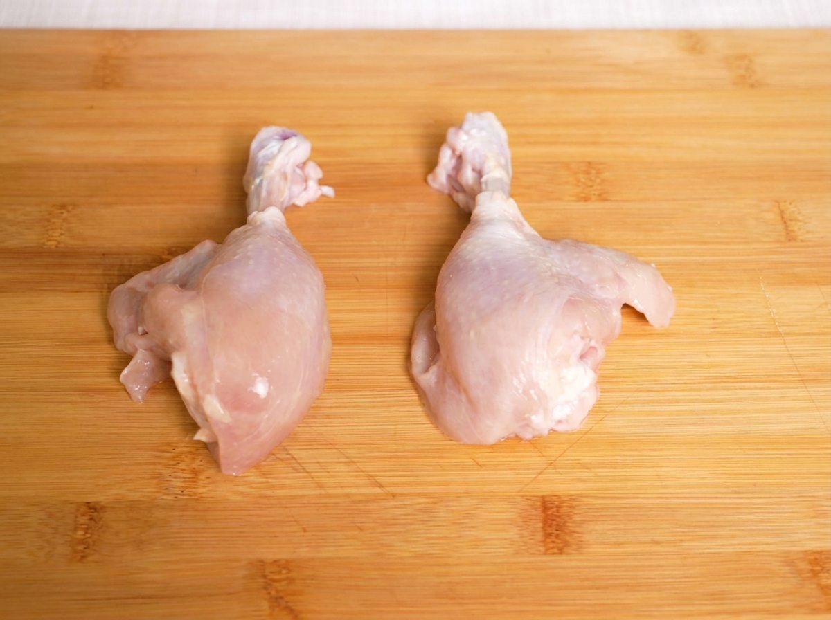 Hauts de cuisse de poulet crus sur une planche à découper, prêts à être tranchés.