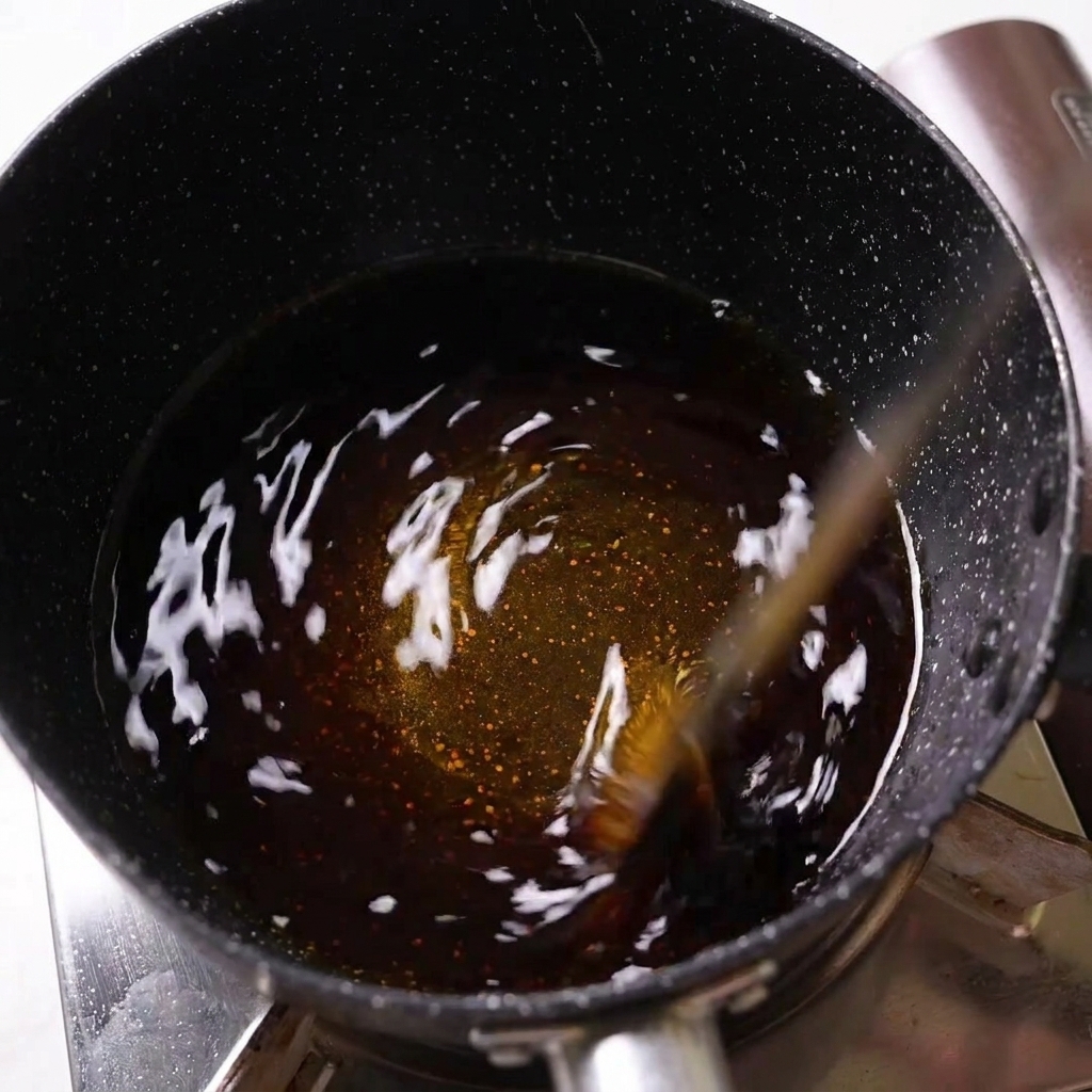 Liquide dassaisonnement sombre remué dans une casserole noire mouchetée sur une cuisinière.