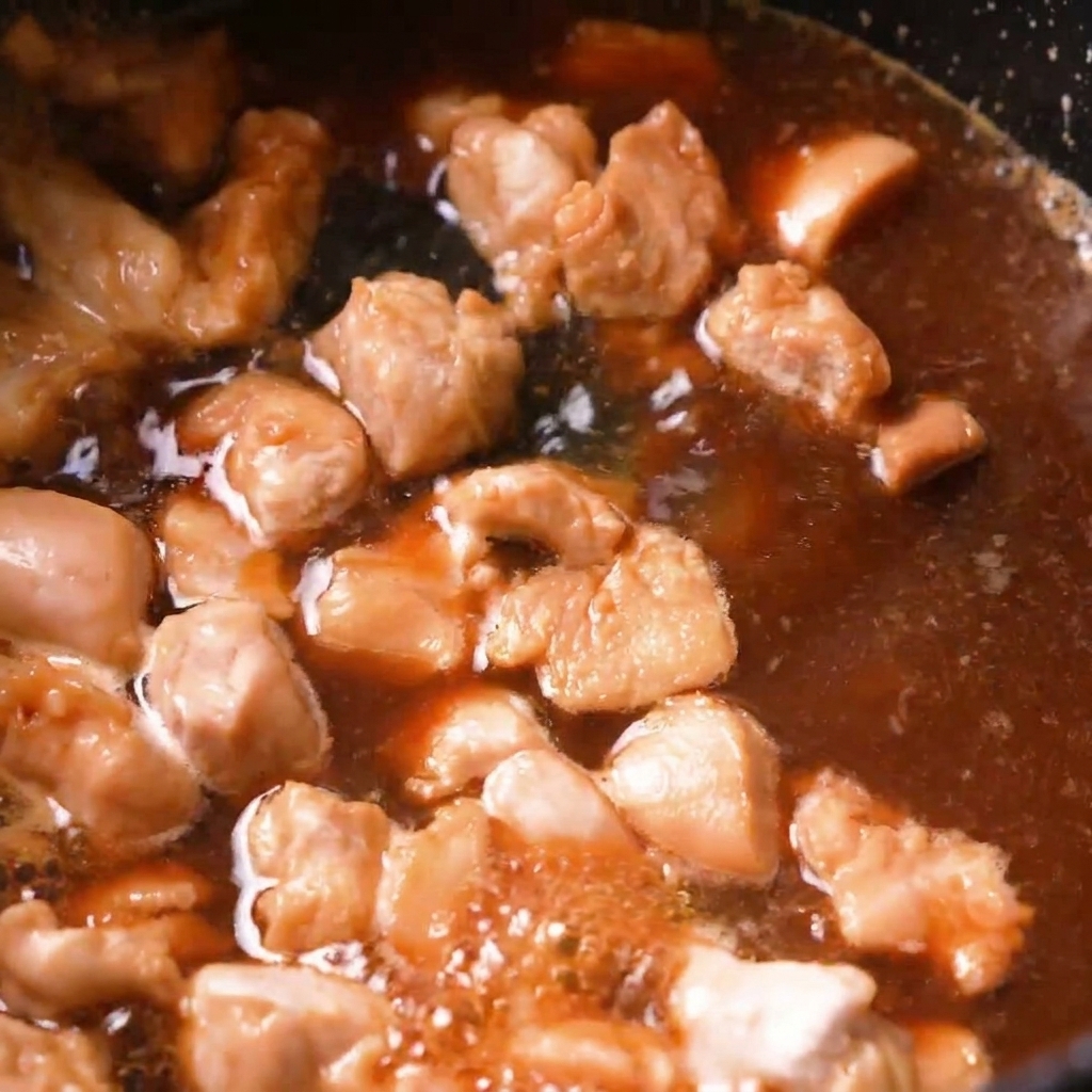 Morceaux de poulet mijotant dans un bouillon dashi brun bouillonnant à lintérieur dune poêle sombre.